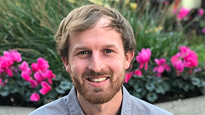 a man smiling in front of a flower bush